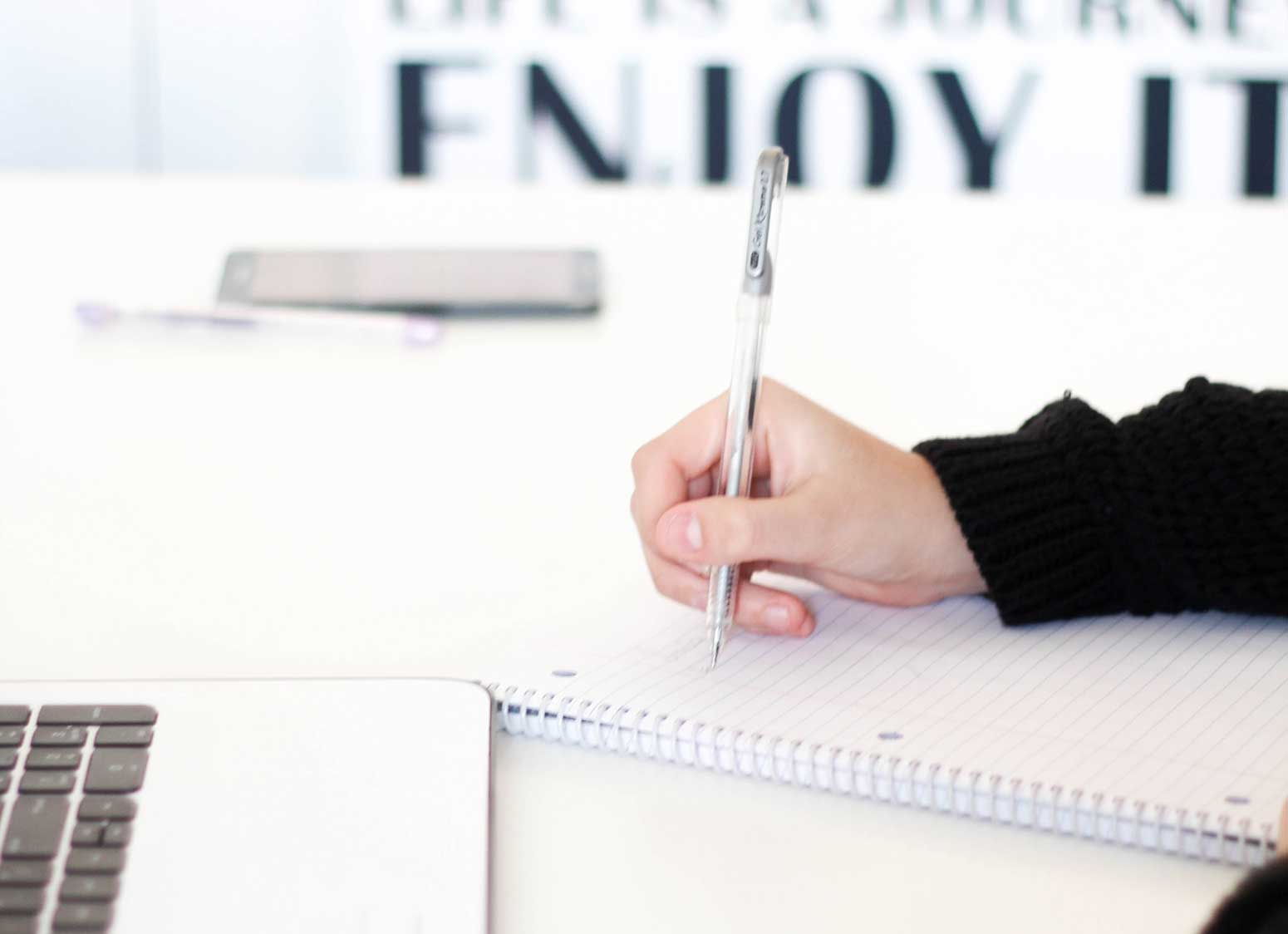 laptop and phone on desk while handwriting notes