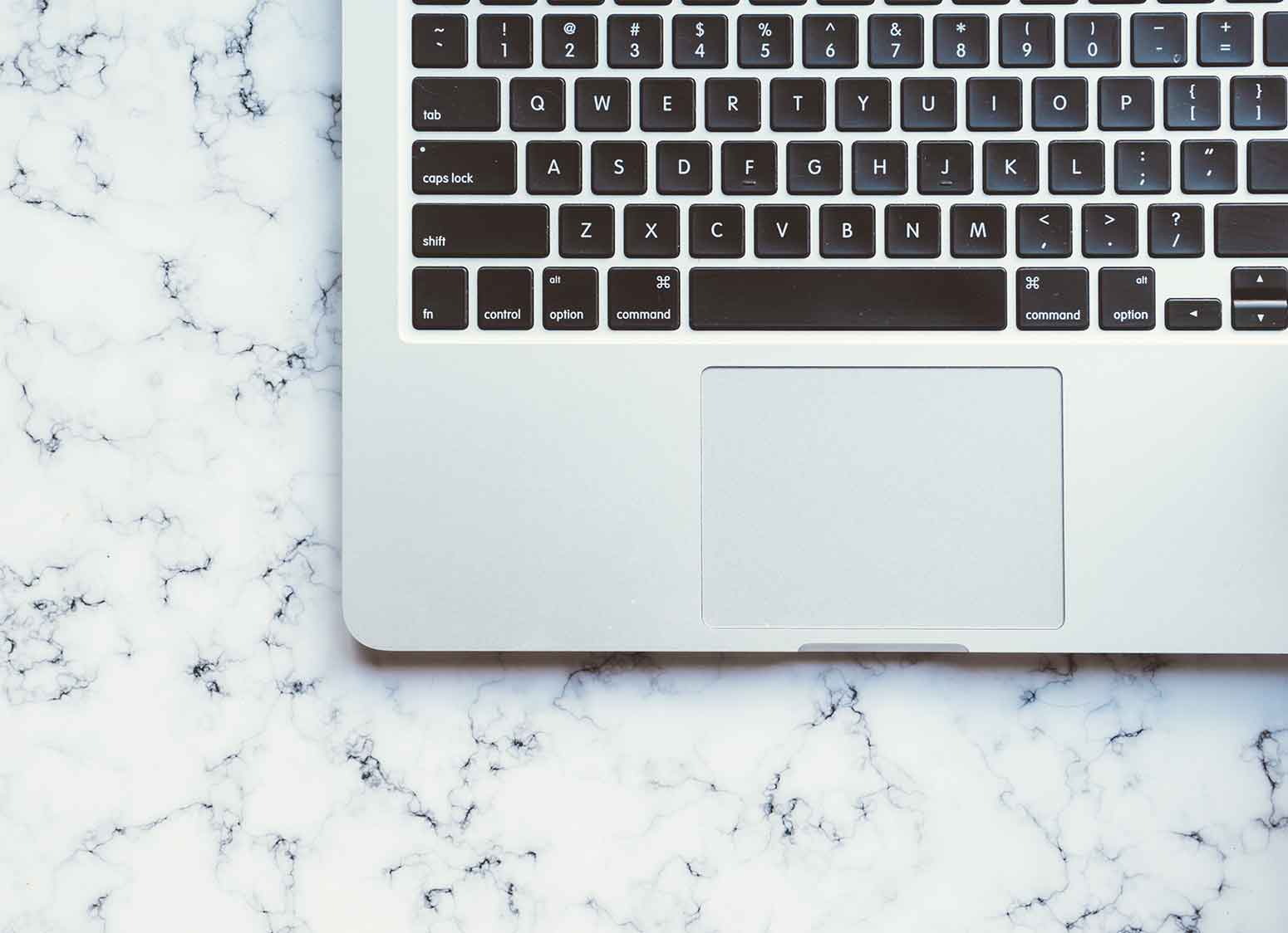 Mac laptop keyboard on marble countertop