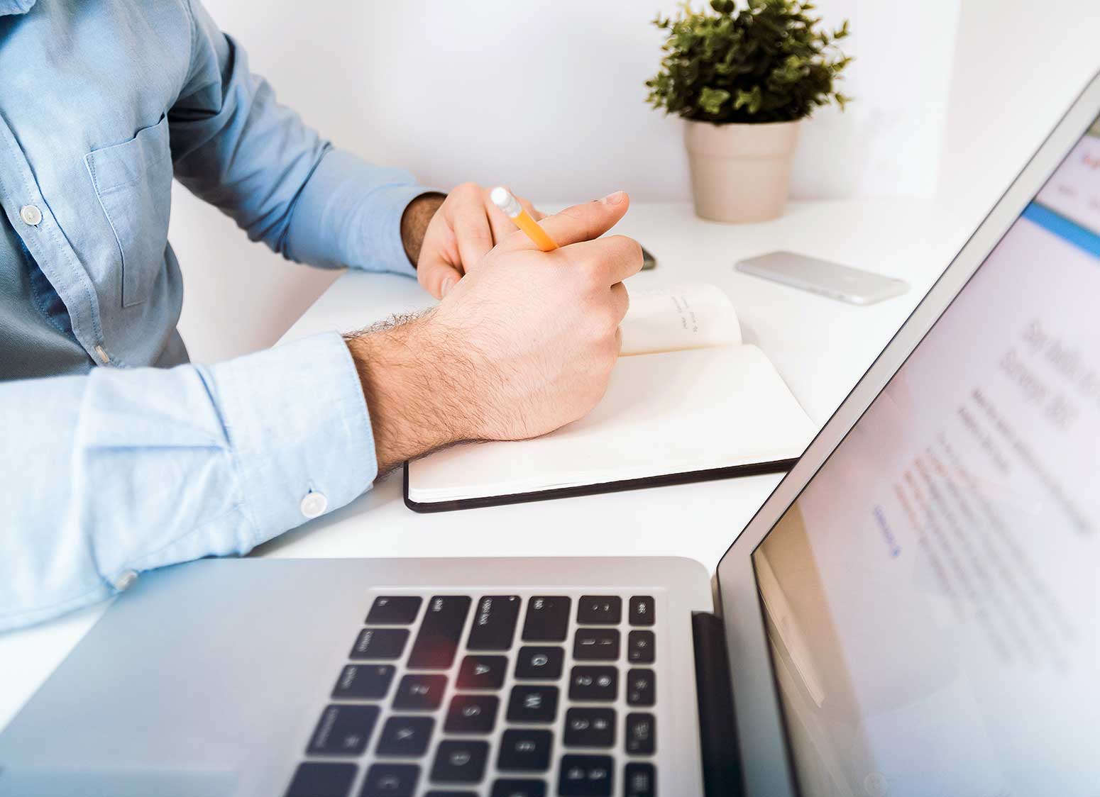 man taking notes next to laptop